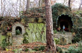 A stone grotto with a statue of the Virgin Mary and plants, surrounded by trees and foliage.
