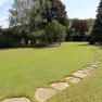 A well-kept garden with a curved stone path and trees in the background.