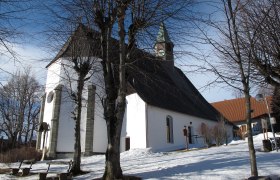 Maria Namen parish church in winter with snow-covered ground and bare trees.