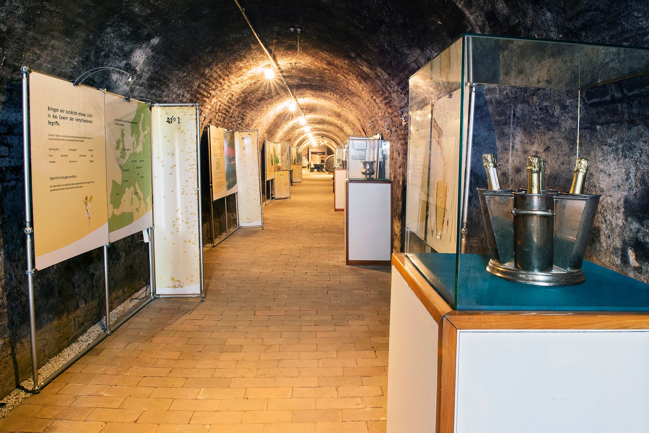 An exhibition room in a wine cellar with information boards and bottles of sparkling wine in tubs.