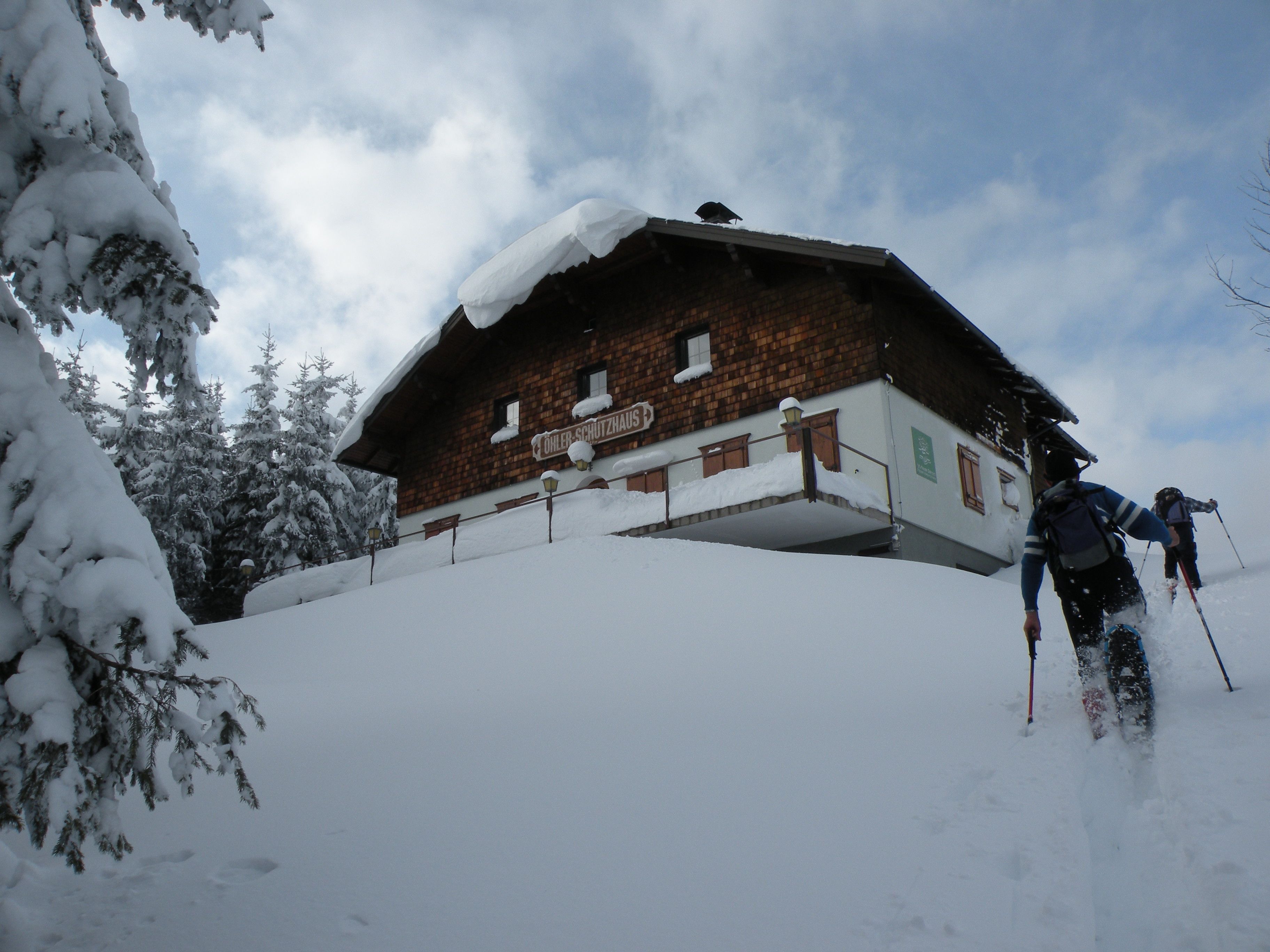 Two people are skiing up a snowy slope to the Öhlerschutzhaus.