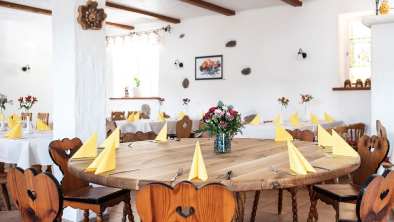 A cozy room with wooden tables and chairs, yellow napkins and flower arrangements.