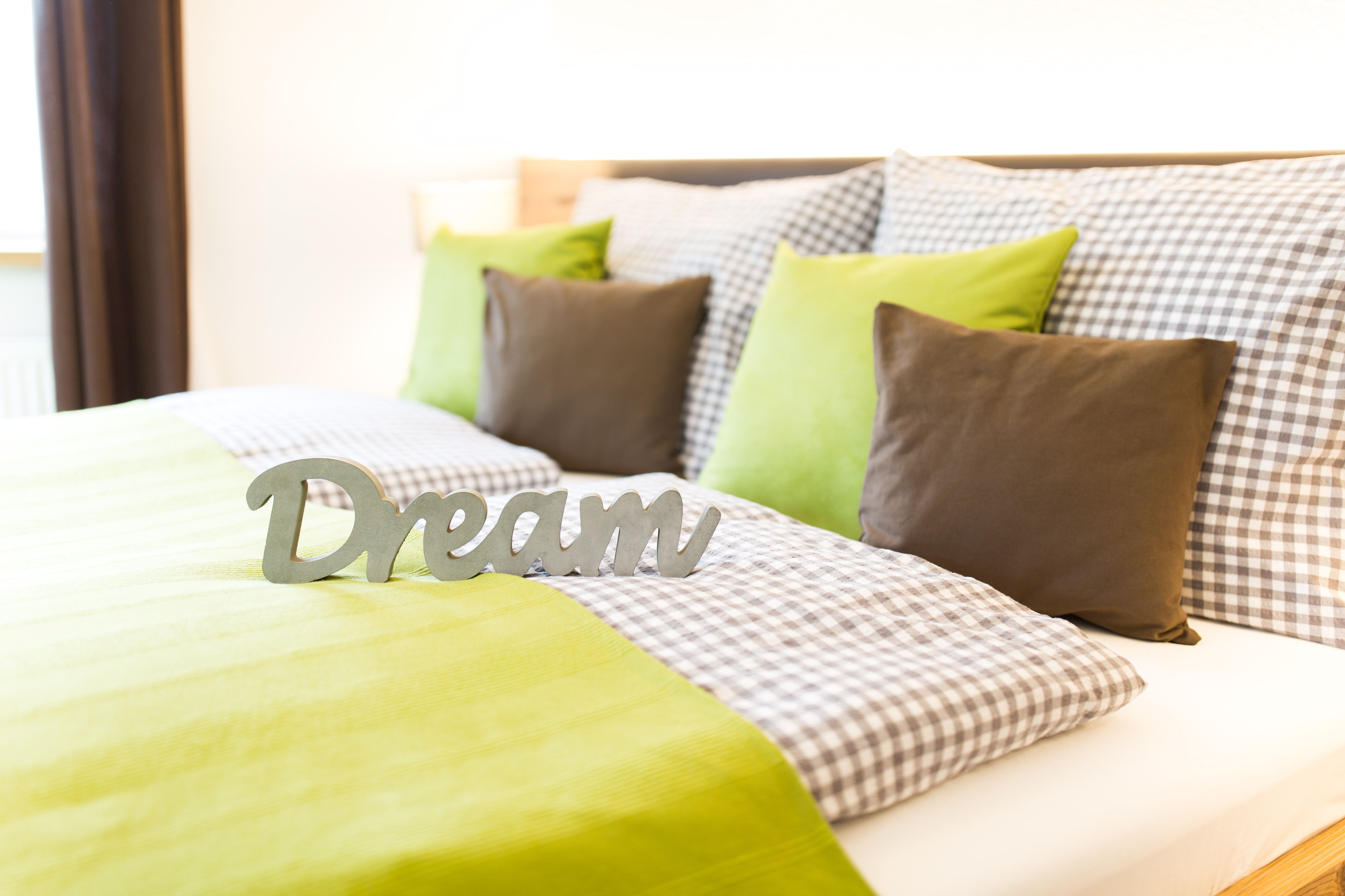Cozy bed with green and checkered bed linen, decorated with pillows and a 'Dream' lettering.