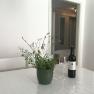 A table with a wine bottle, a wine glass and a plant in a room.