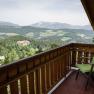 View from a balcony of a mountain landscape with forests and a building in the distance.