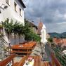 Terrace with wooden benches and tables, view of rooftops and mountains in the background.