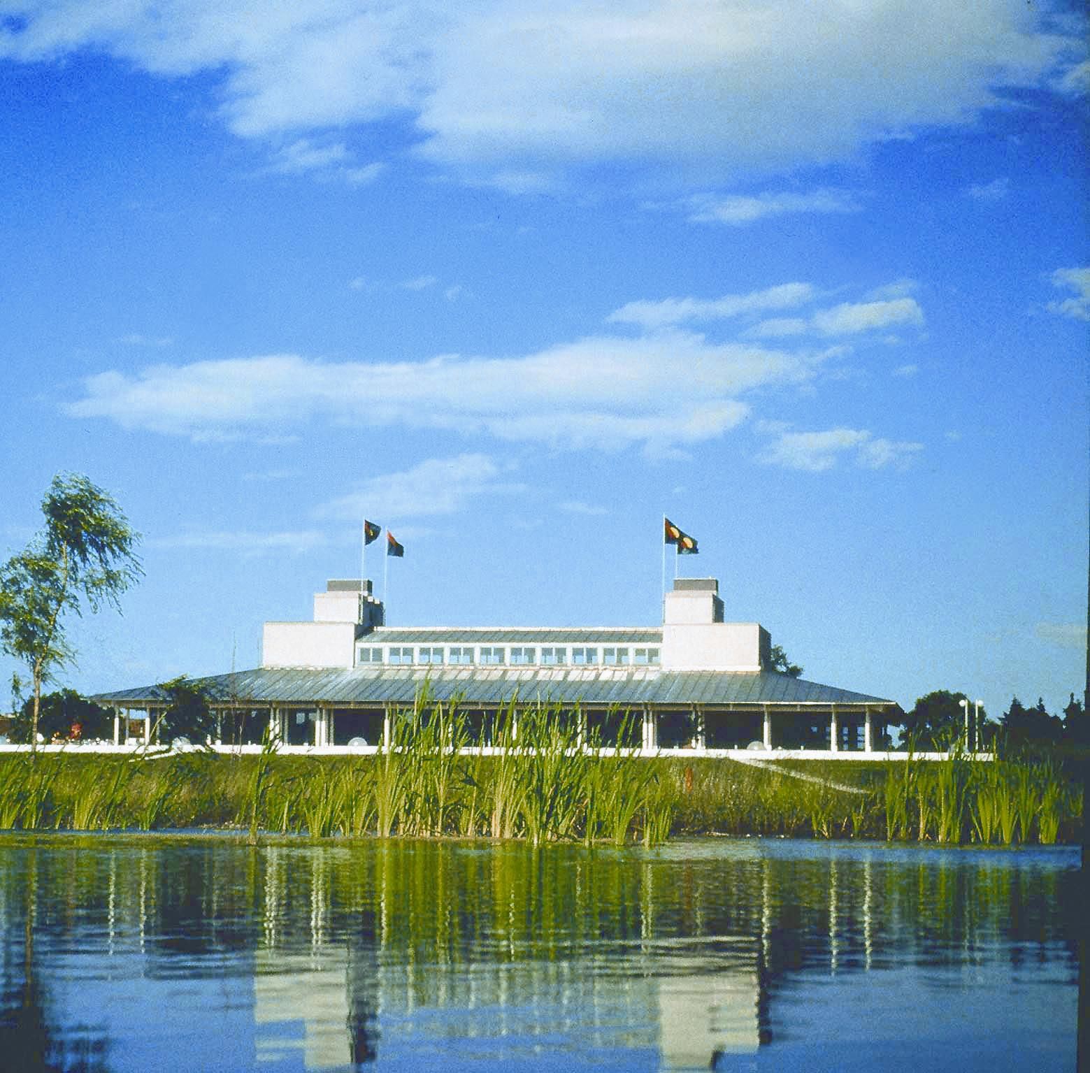 Building of the Golf Club Schloss Ebreichsdorf behind a pond with reeds, blue sky.