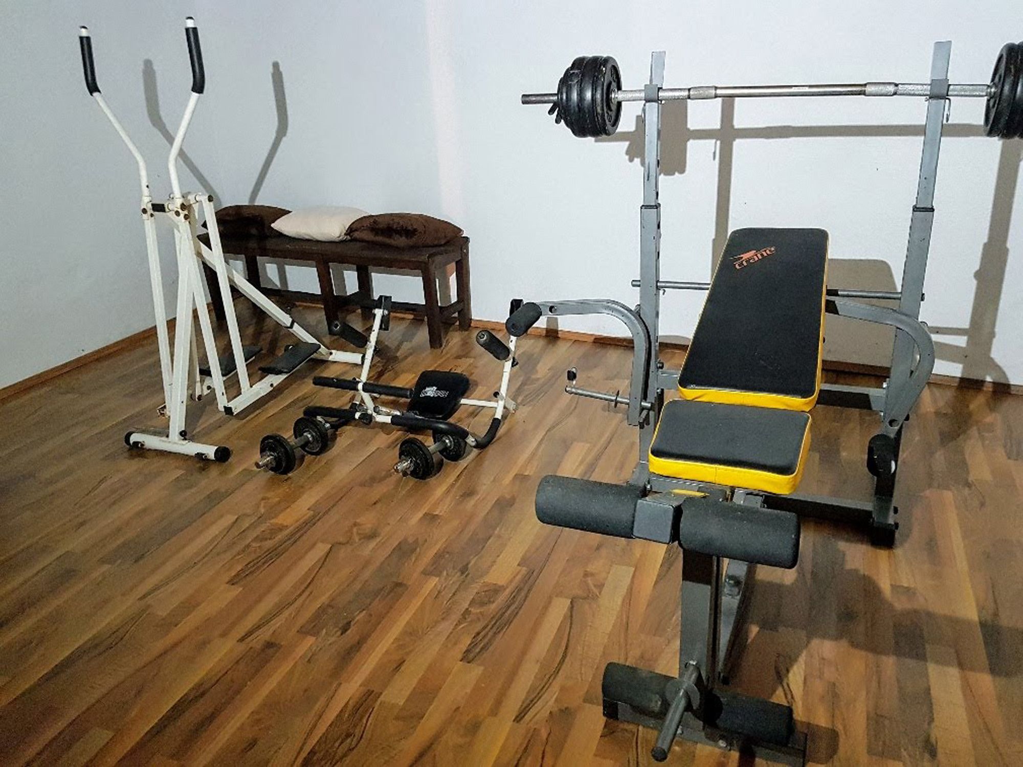 A fitness room with weight bench, cross trainer and dumbbells on a wooden floor.