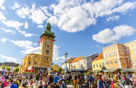 Crowd on a busy square in Retz with a striking clock tower in the background.