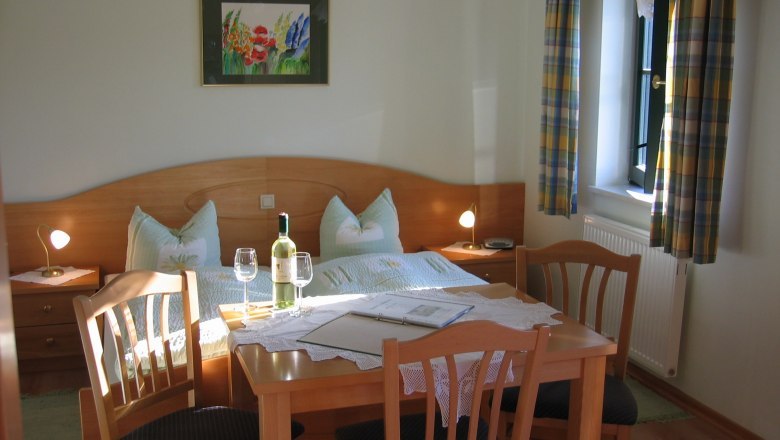 Cozy guest room with double bed, table and chairs, wine bottle and glasses, window with curtains.