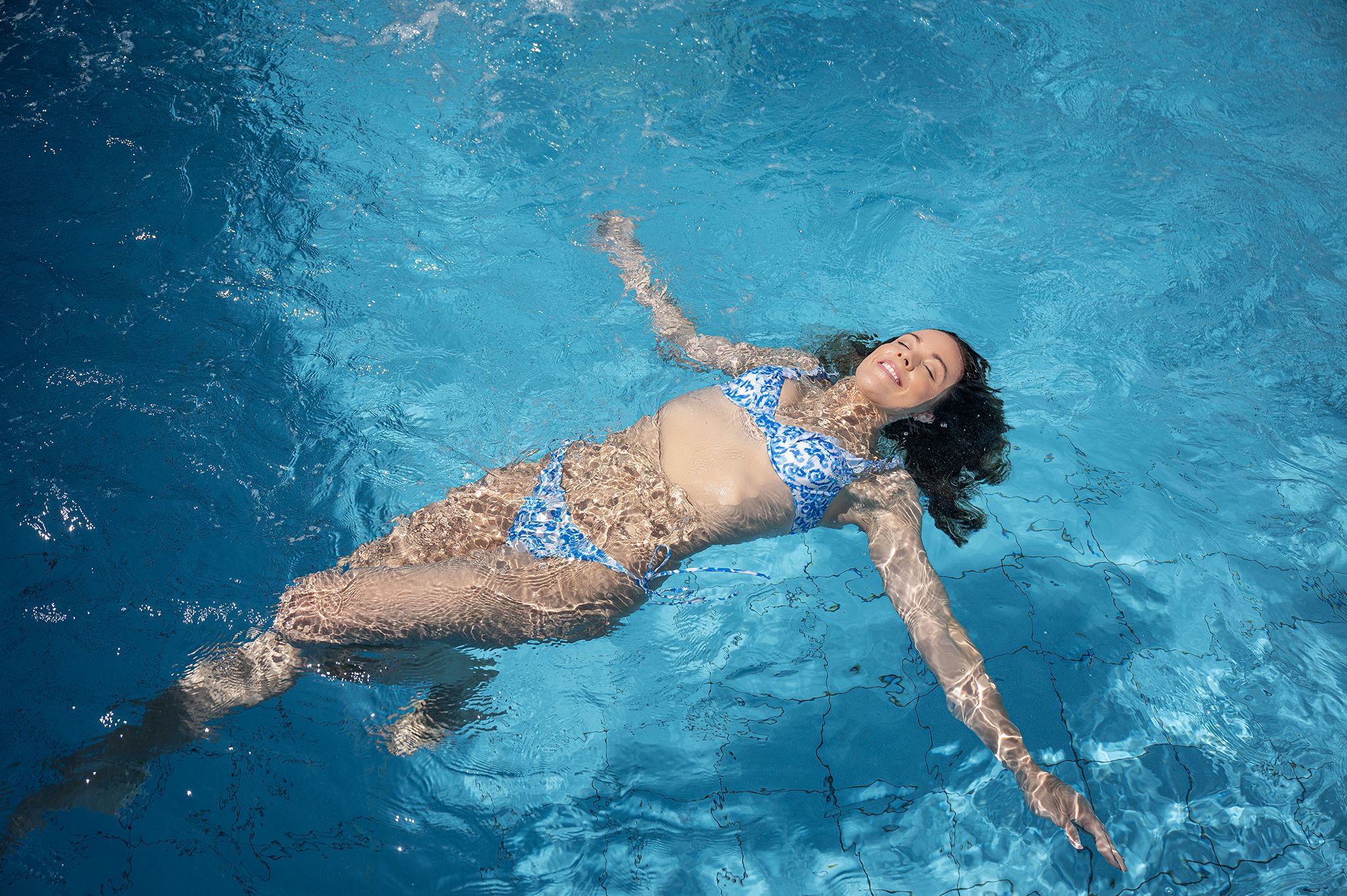 Woman in blue bikini floating relaxed in the pool.
