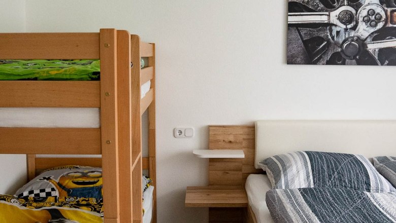 A bedroom with a bunk bed and a double bed made of wood. A picture with a technical motif hangs on the wall.