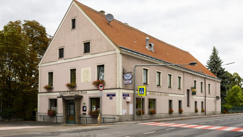 A traditional pub with a pink fa&ccedil;ade and red roof tiles on a street corner in Pottenbrunn.