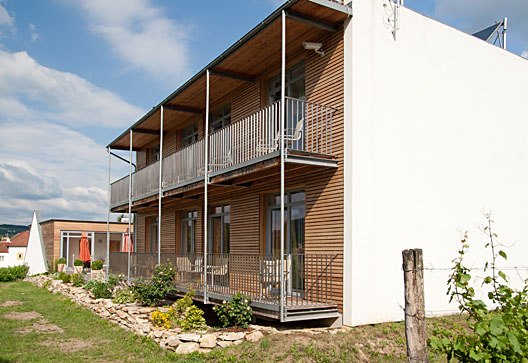 Modern building with wooden facade and balconies, surrounded by garden.