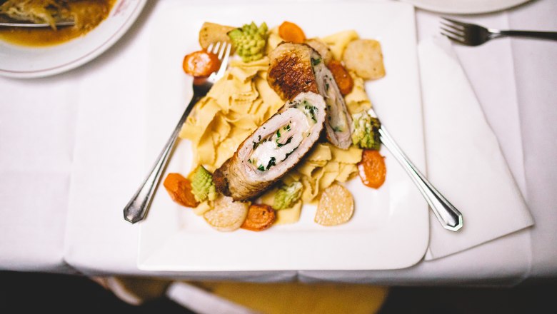 Stuffed meat on noodles with vegetables on a white plate.