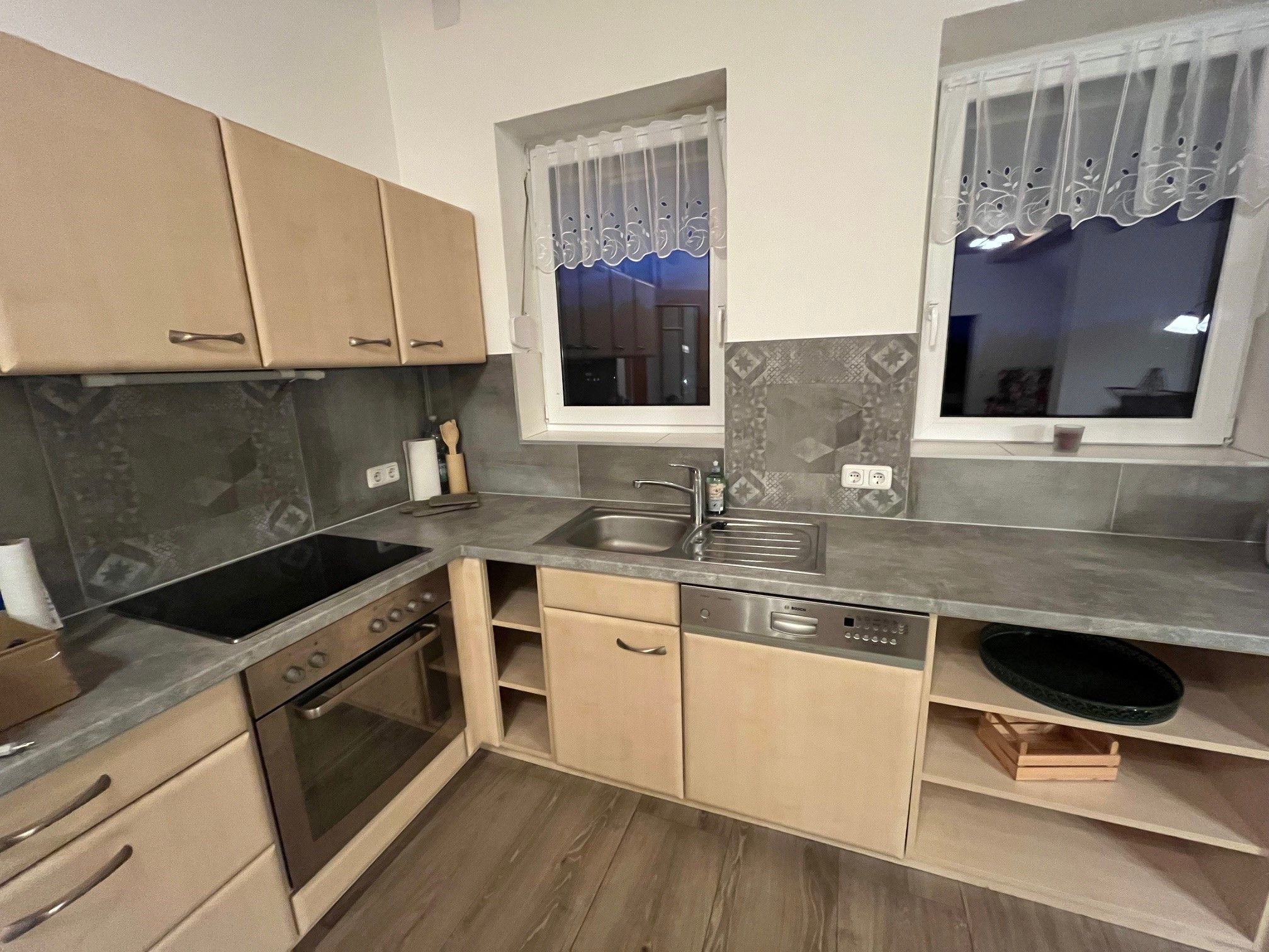 Modern kitchen with wooden cupboards, electric stove, sink and dishwasher.