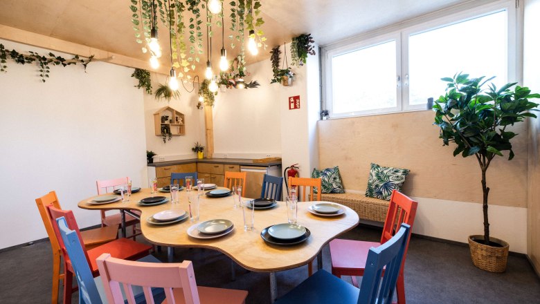A cozy room with a table surrounded by colorful chairs and plants.