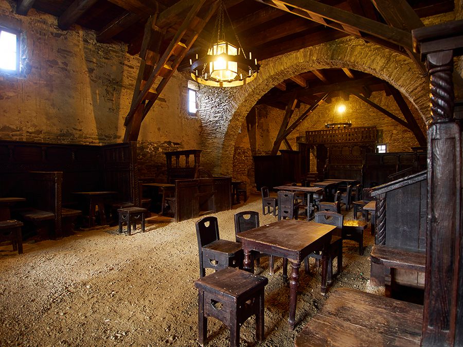 Interior view of a medieval tavern with wooden furniture and stone walls.
