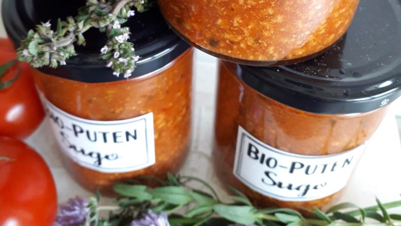 Jars of organic turkey sugo, next to tomatoes and herbs.