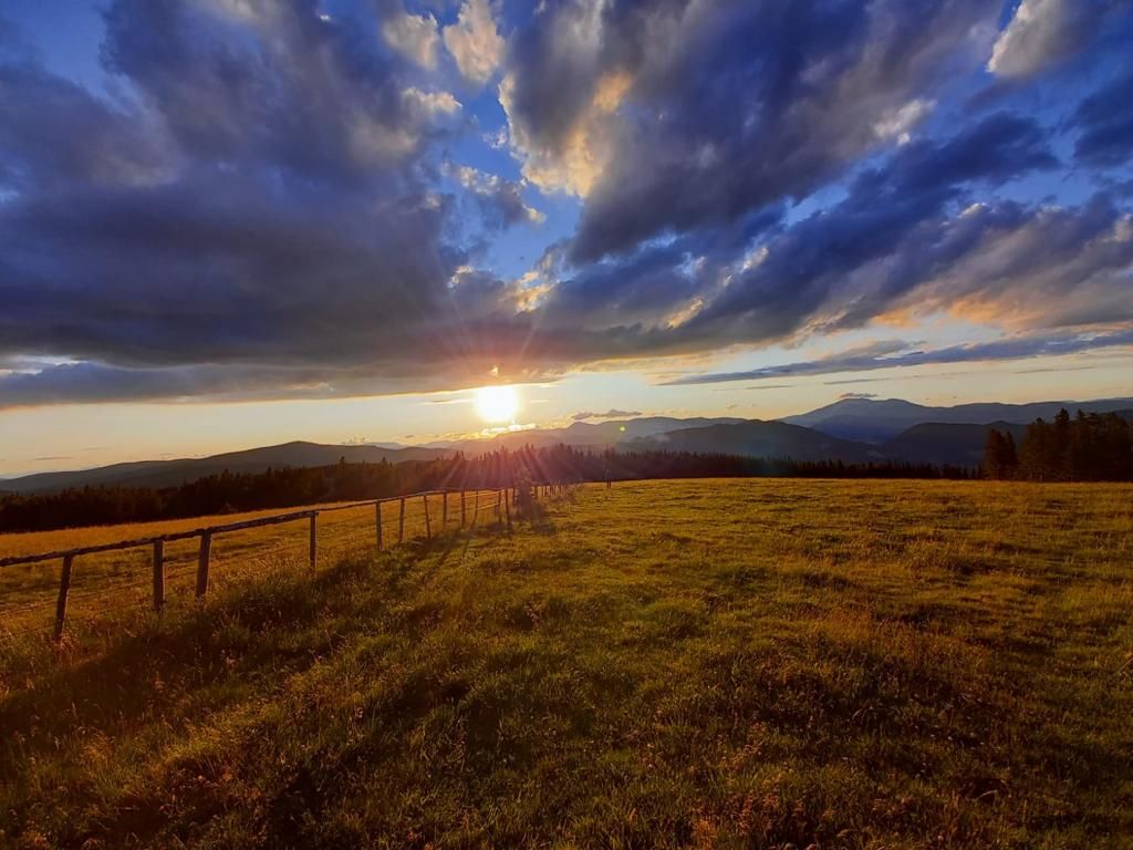 Sunset over a green meadow with mountains in the background and dramatic clouds in the sky.