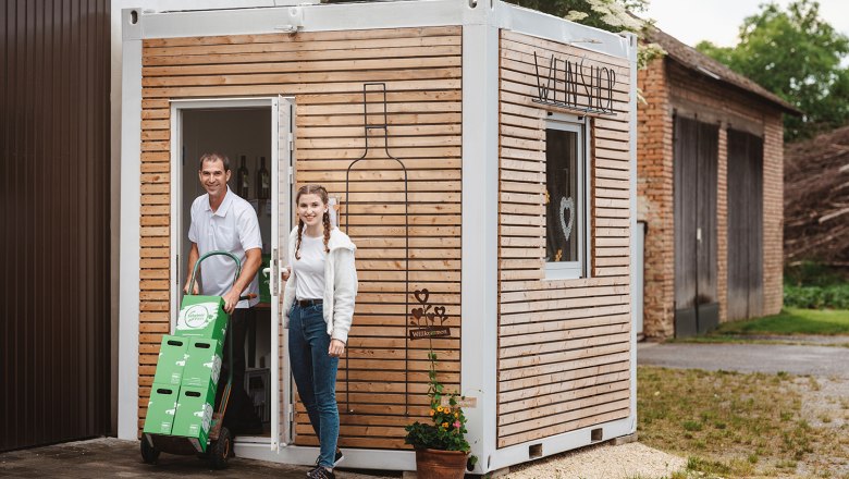 Two people in front of a small wooden building labeled 'Weinshop'.
