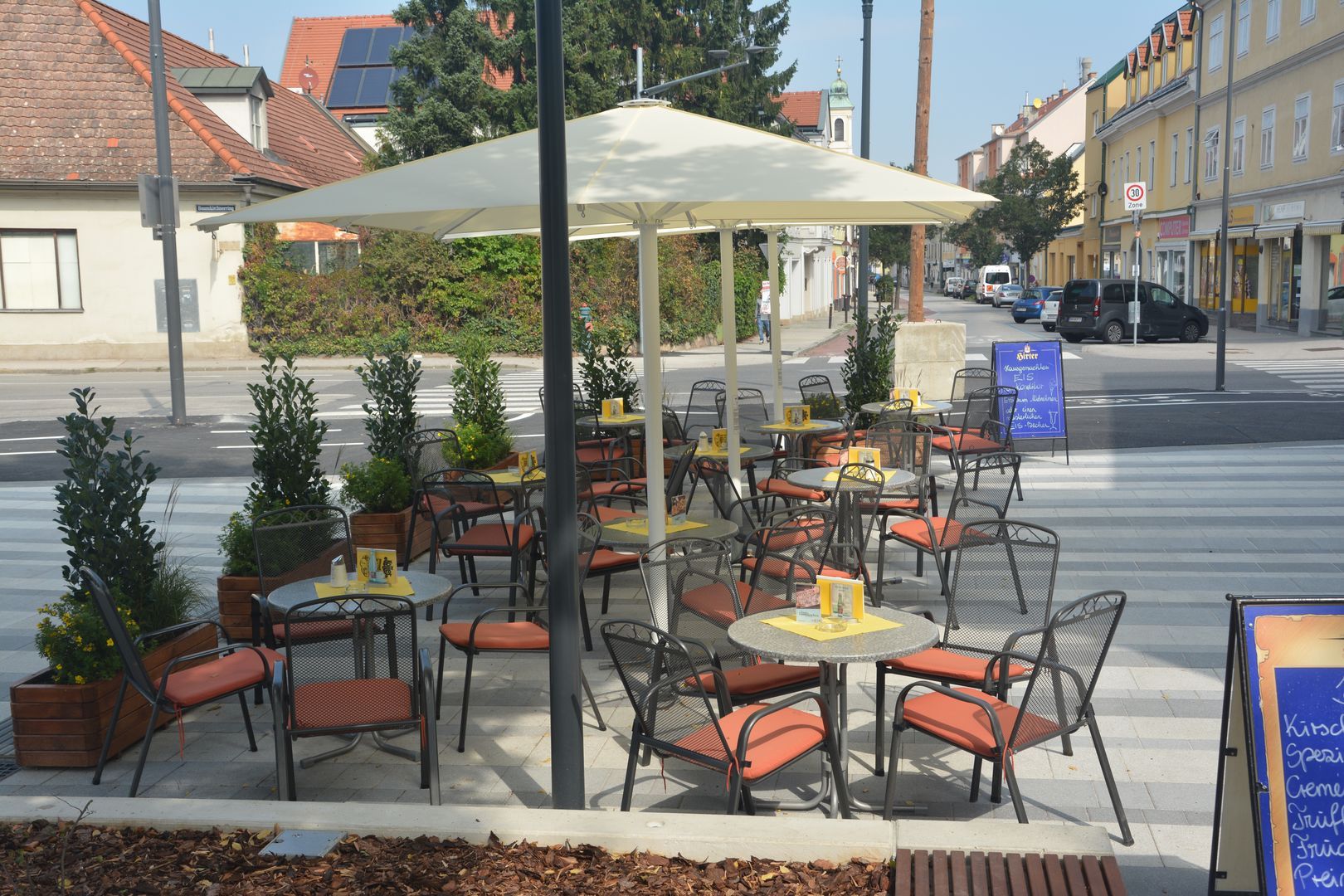 An empty pavement garden with tables, chairs and parasols on a paved area in an urban environment.
