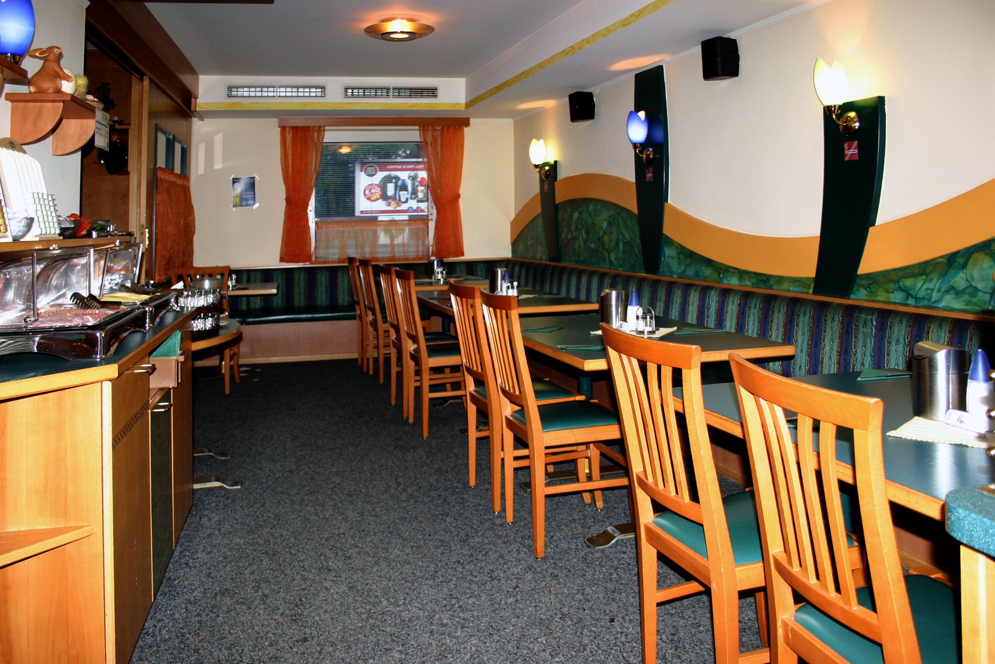 Interior view of an empty restaurant with wooden furniture and green upholstery.