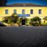 Yellow building with the inscription 'Auland-Hotel Siebenbrunnerhof', surrounded by trees and an old car.