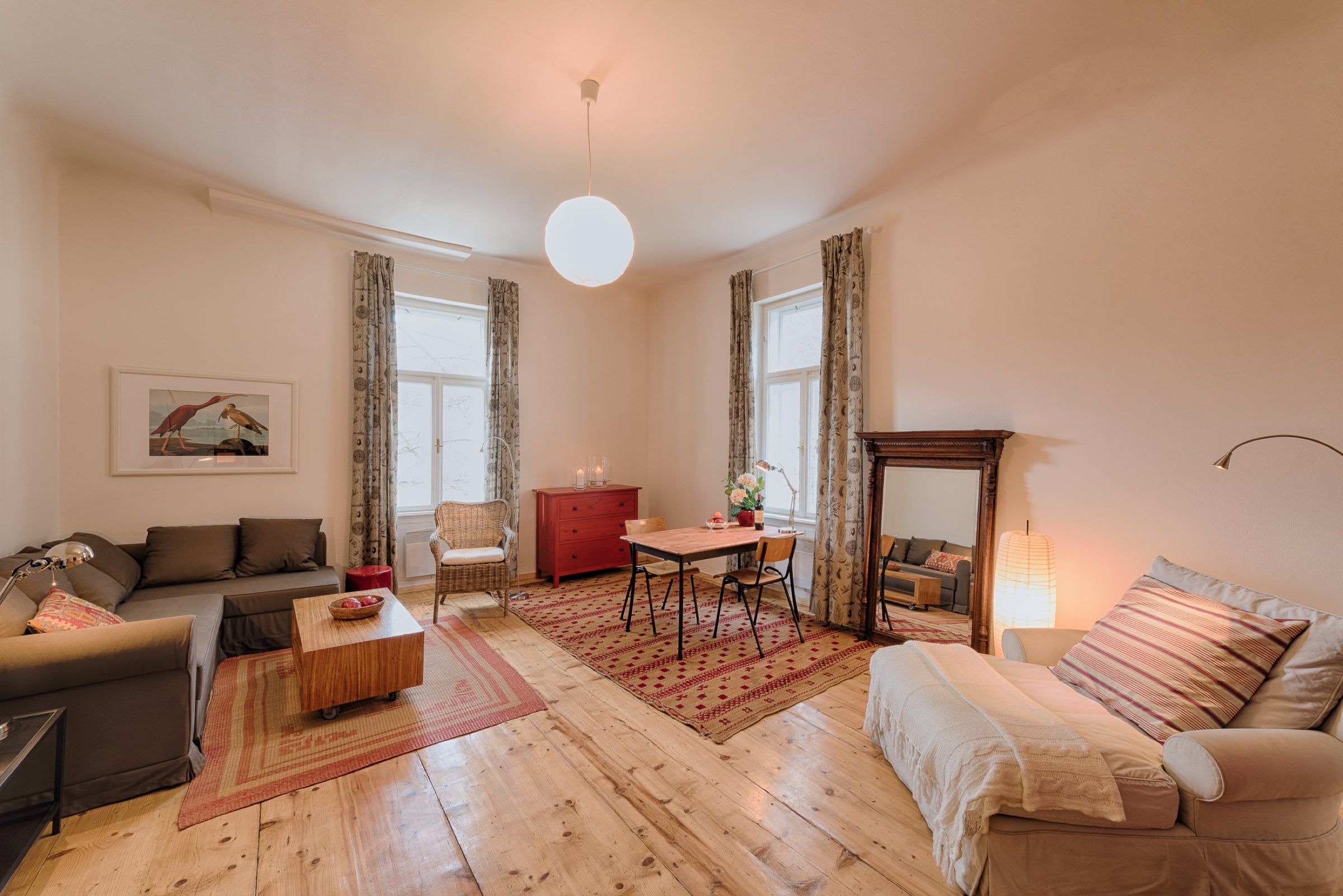 Cozy living room with wooden floor, sofa, armchair, dining table and large mirror.