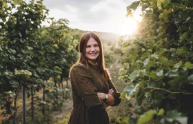 Frau, welche zwischen Weinreben steht.
