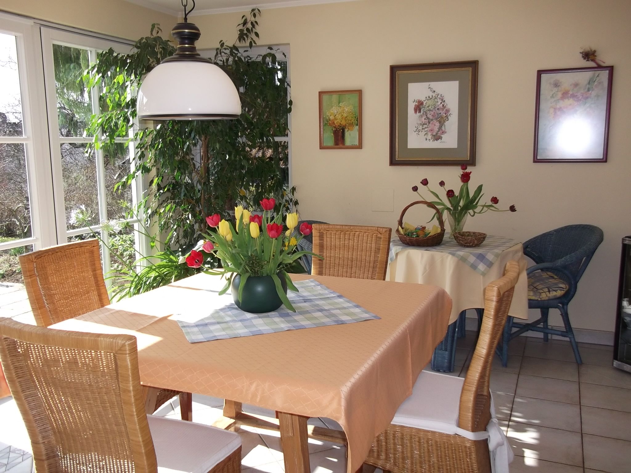 A cozy dining area with a table holding a bouquet of flowers, surrounded by wicker chairs and decorative pictures on the wall.