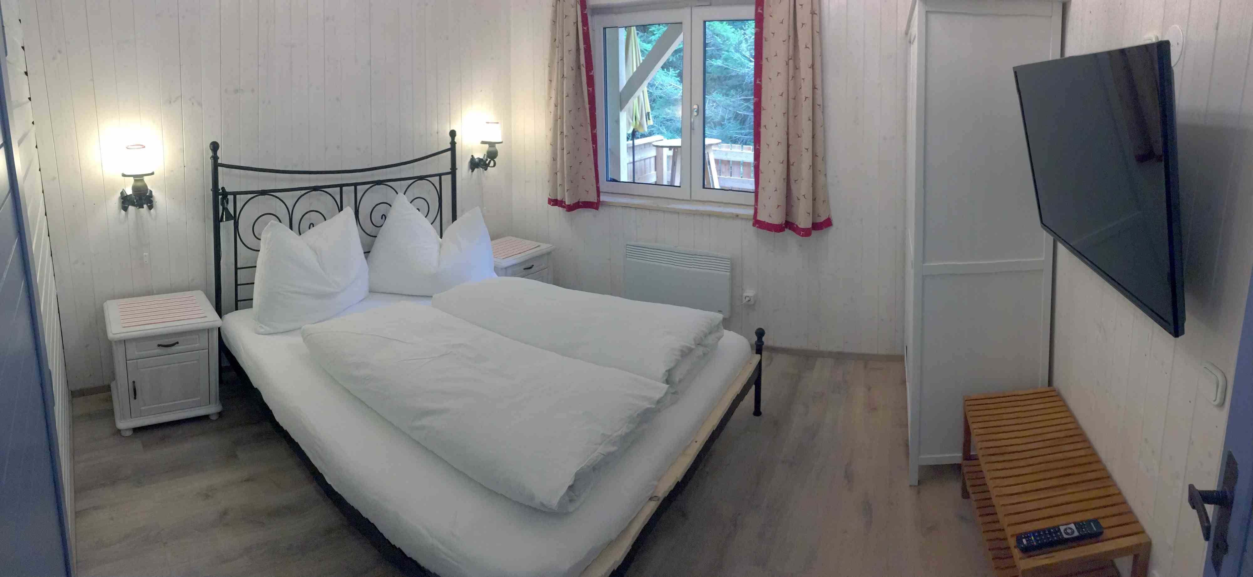 Bedroom in a vacation home with double bed, TV and window with curtains.
