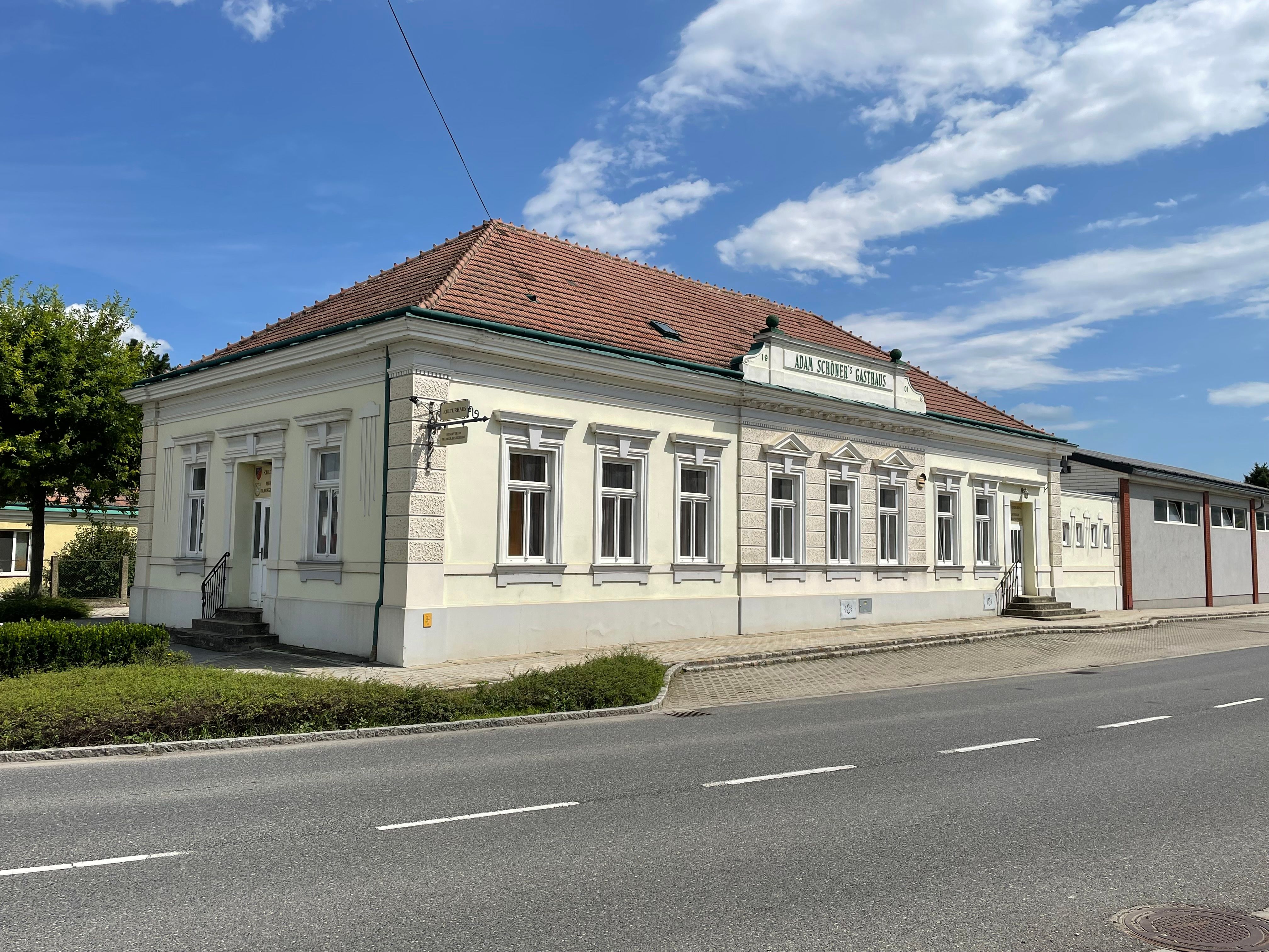 The Kulturhaus, a bright historic building with a red-tiled roof, stands on a street beneath a blue sky.