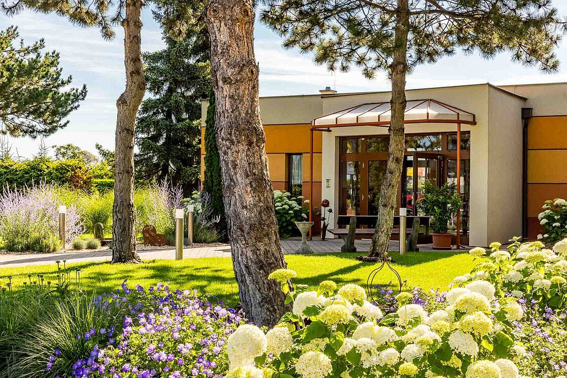 Entrance to a modern building with garden and trees.