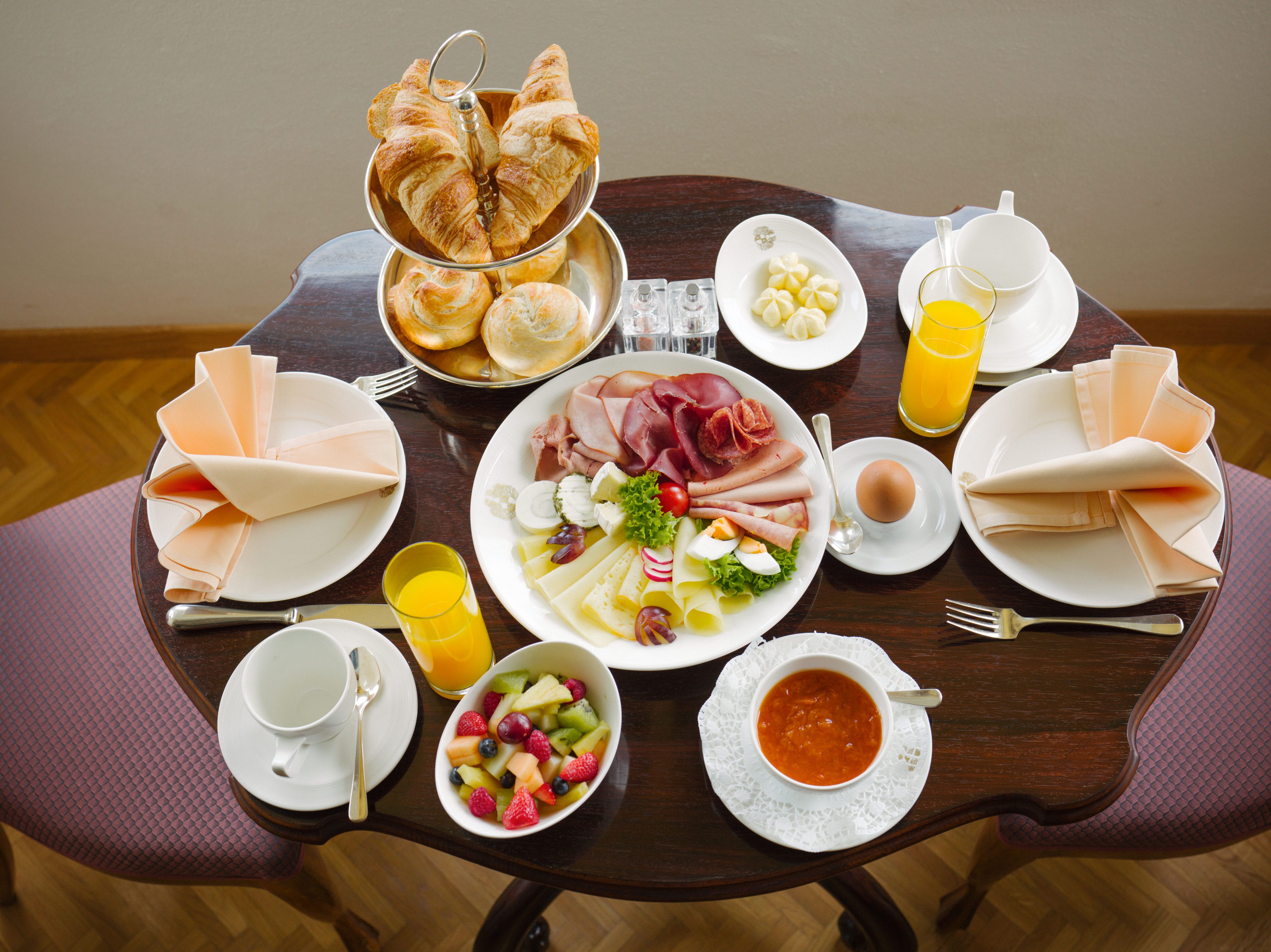 Breakfast table with croissants, bread rolls, cold cuts, cheese, fruit salad, orange juice and coffee.