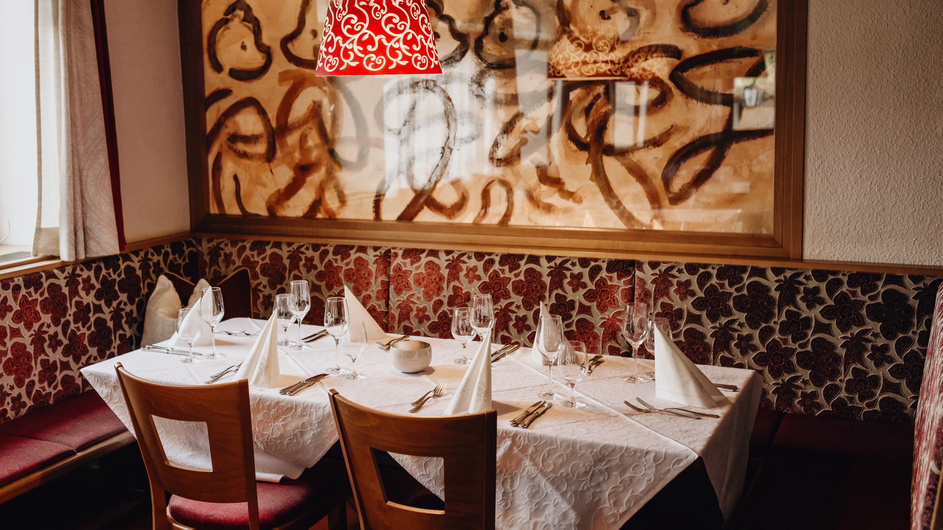 A stylishly laid table in a restaurant with art on the wall and a red lamp.
