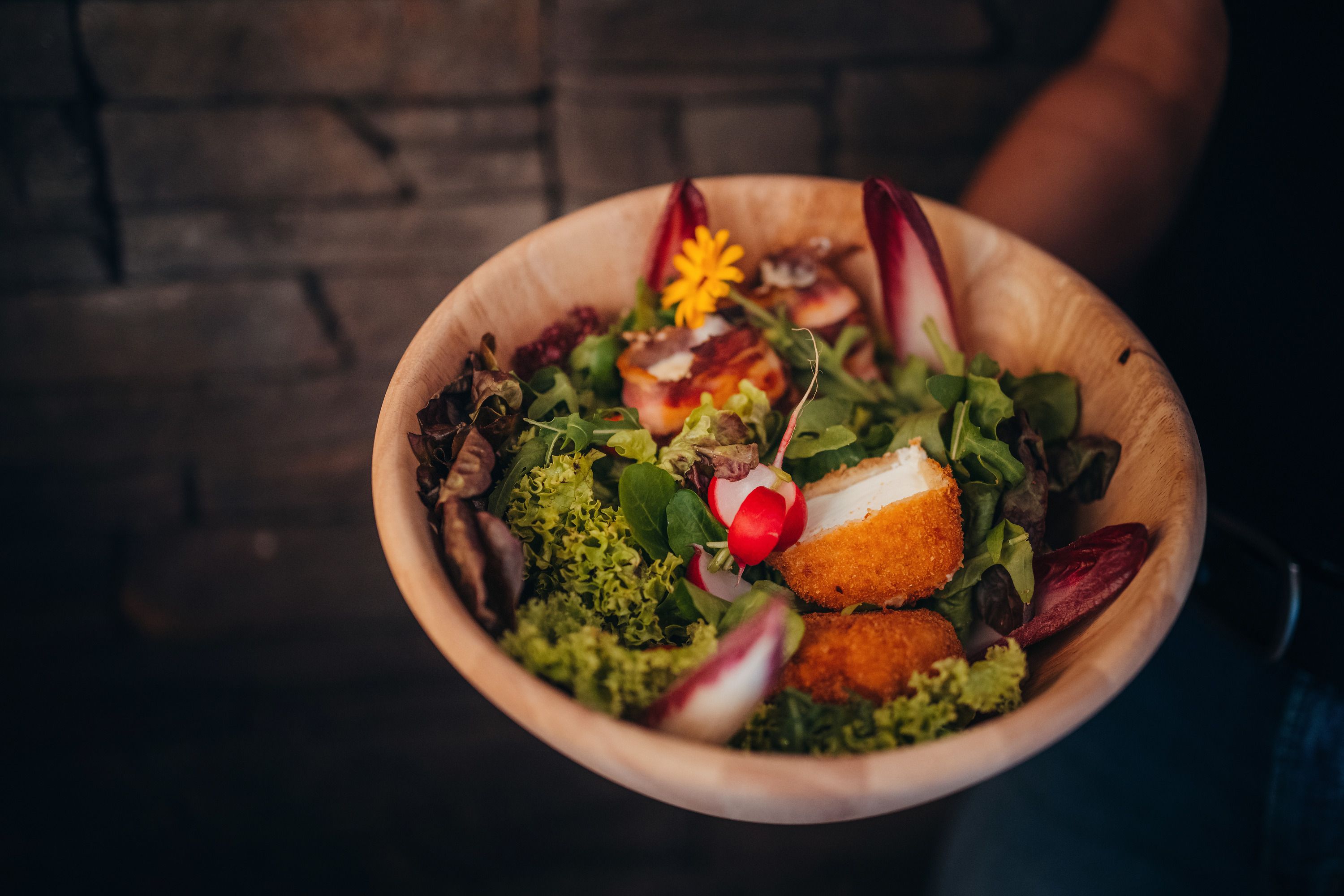 Wooden bowl with lettuce, baked sheep's cheese and radishes.
