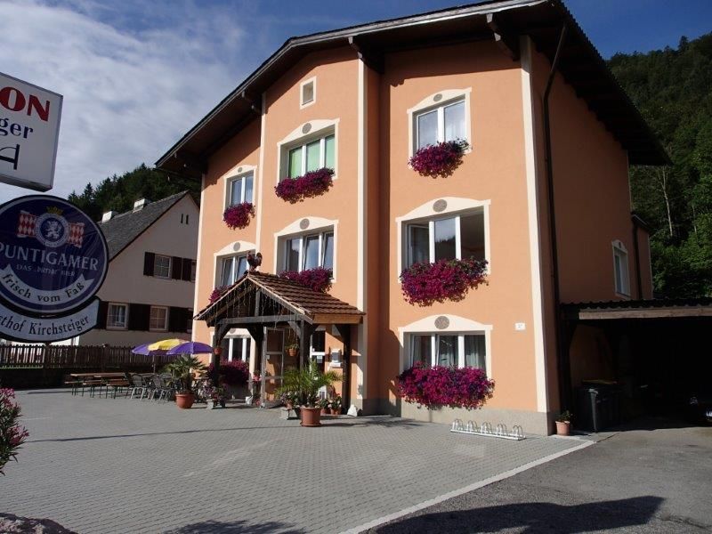 A three-storey building with an orange façade and flower boxes in front of the windows. A sign with the inscription 'Puntigamer' is visible.