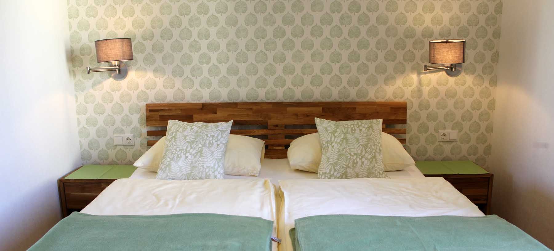 Cozy room with double bed, patterned wallpaper, wall lamps, bedside tables and pillows.
