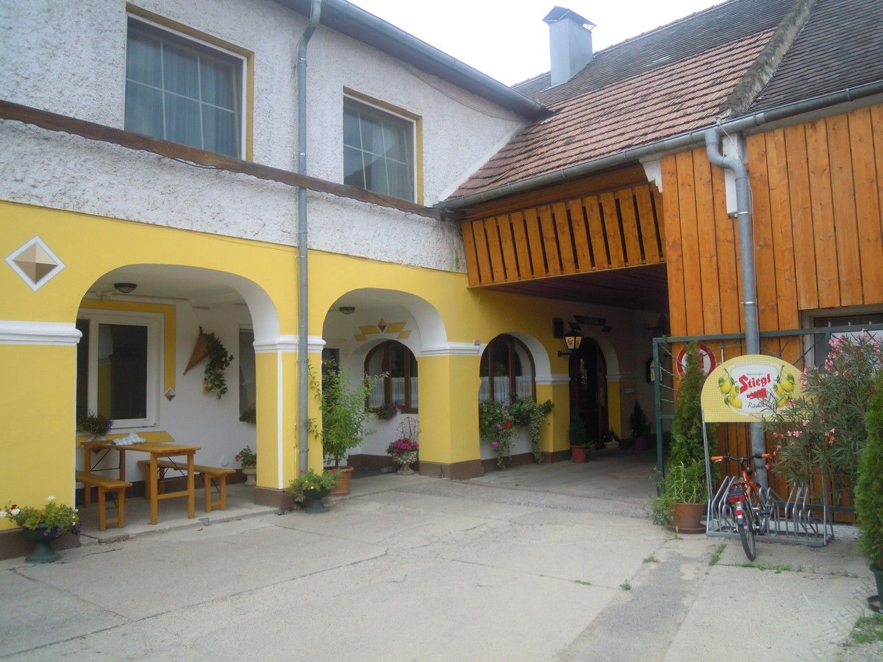 A yellow arcaded courtyard with a wooden roof and plants.