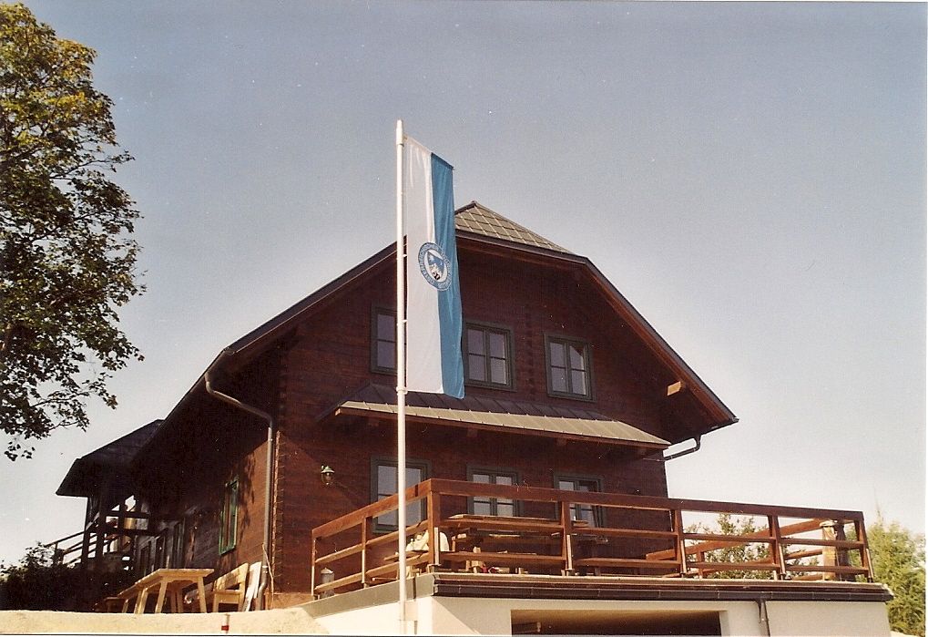 Wooden hut with flag on terrace, blue sky.