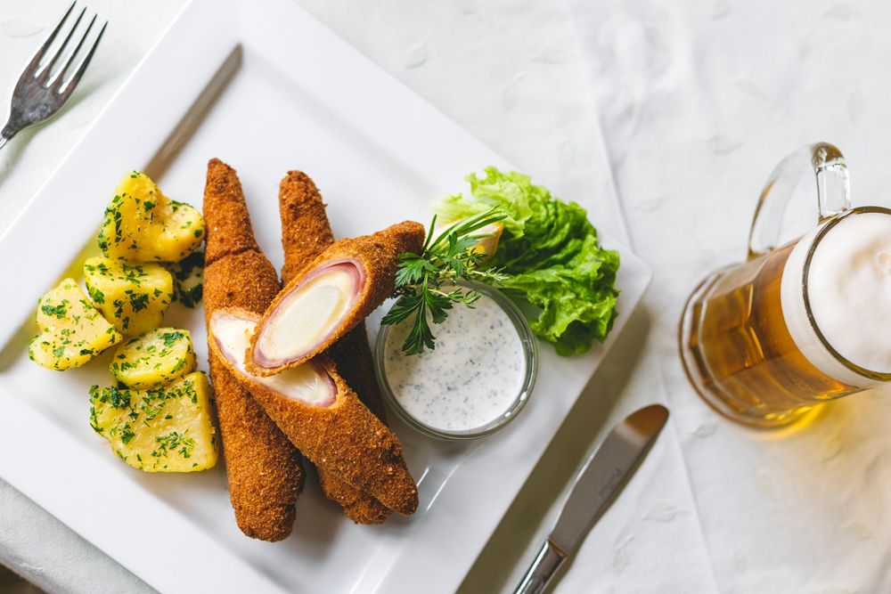 Baked asparagus with potatoes, salad and beer on a white plate.
