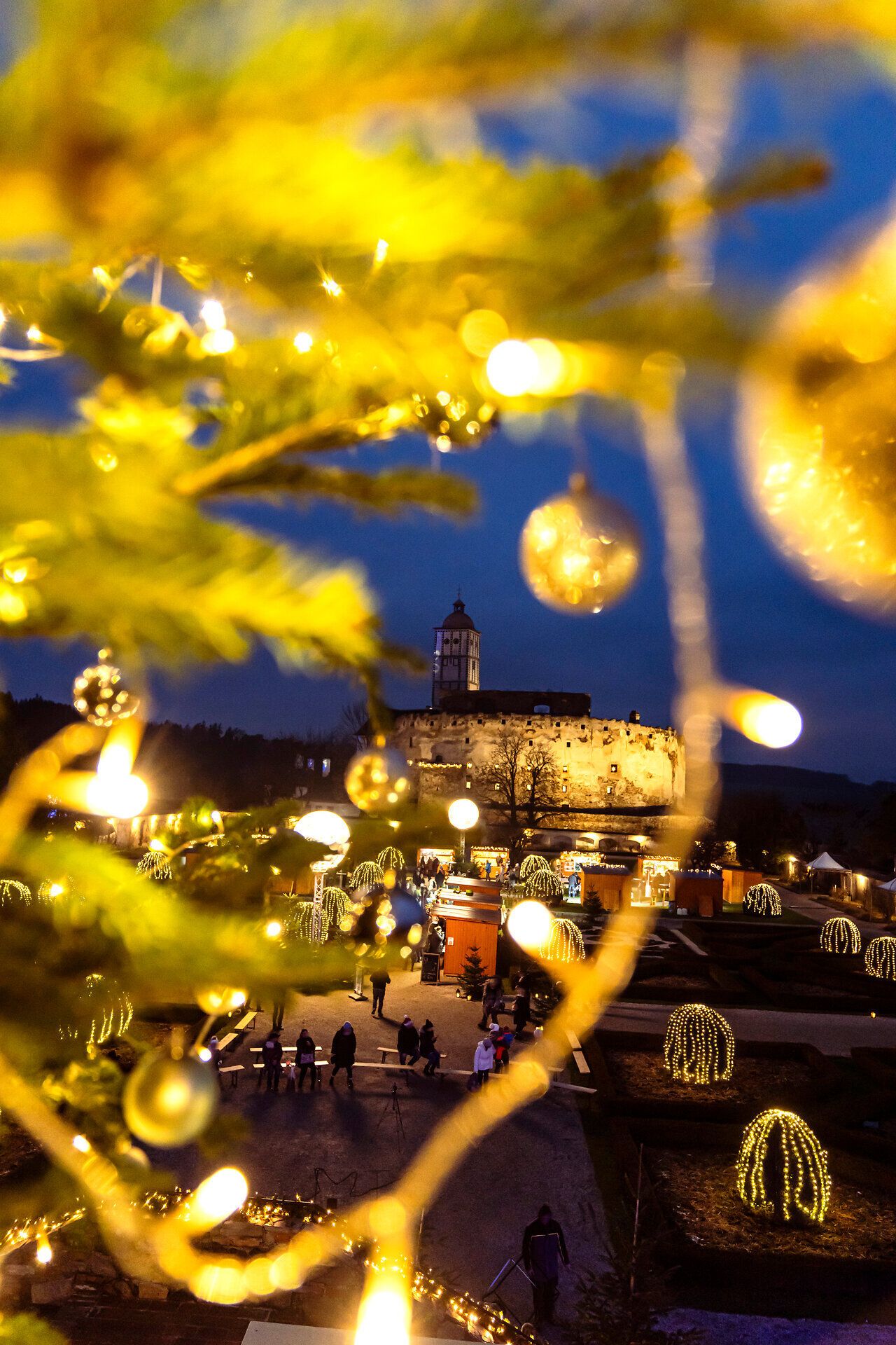 In der festlich geschmückten Adventszeit erstrahlt die Umgebung in warmem Licht, während die sanften Hügel im Hintergrund eine malerische Kulisse bieten. Glitzernde Weihnachtsdekorationen und der Duft von frisch gebrannten Mandeln laden zum Verweilen ein und versetzen die Besucher in eine besinnliche Stimmung.