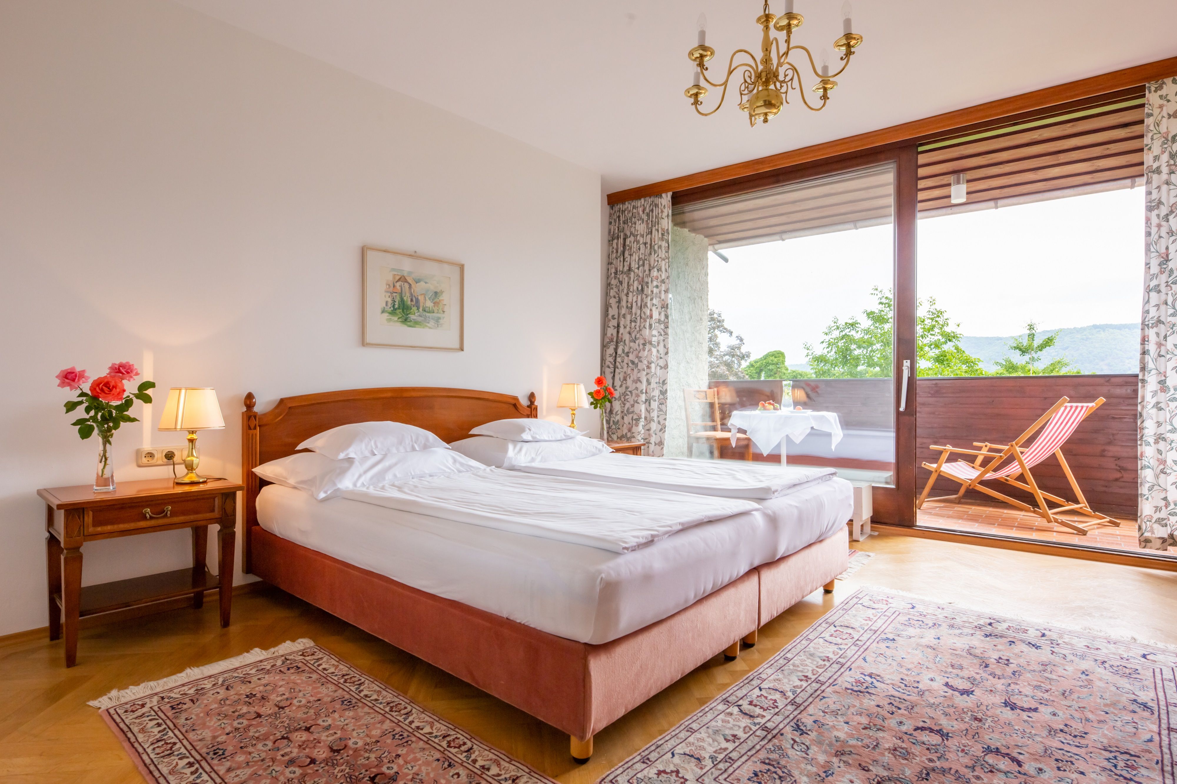 A cozy bedroom with double bed, bedside lamps and balcony with deck chair and table.