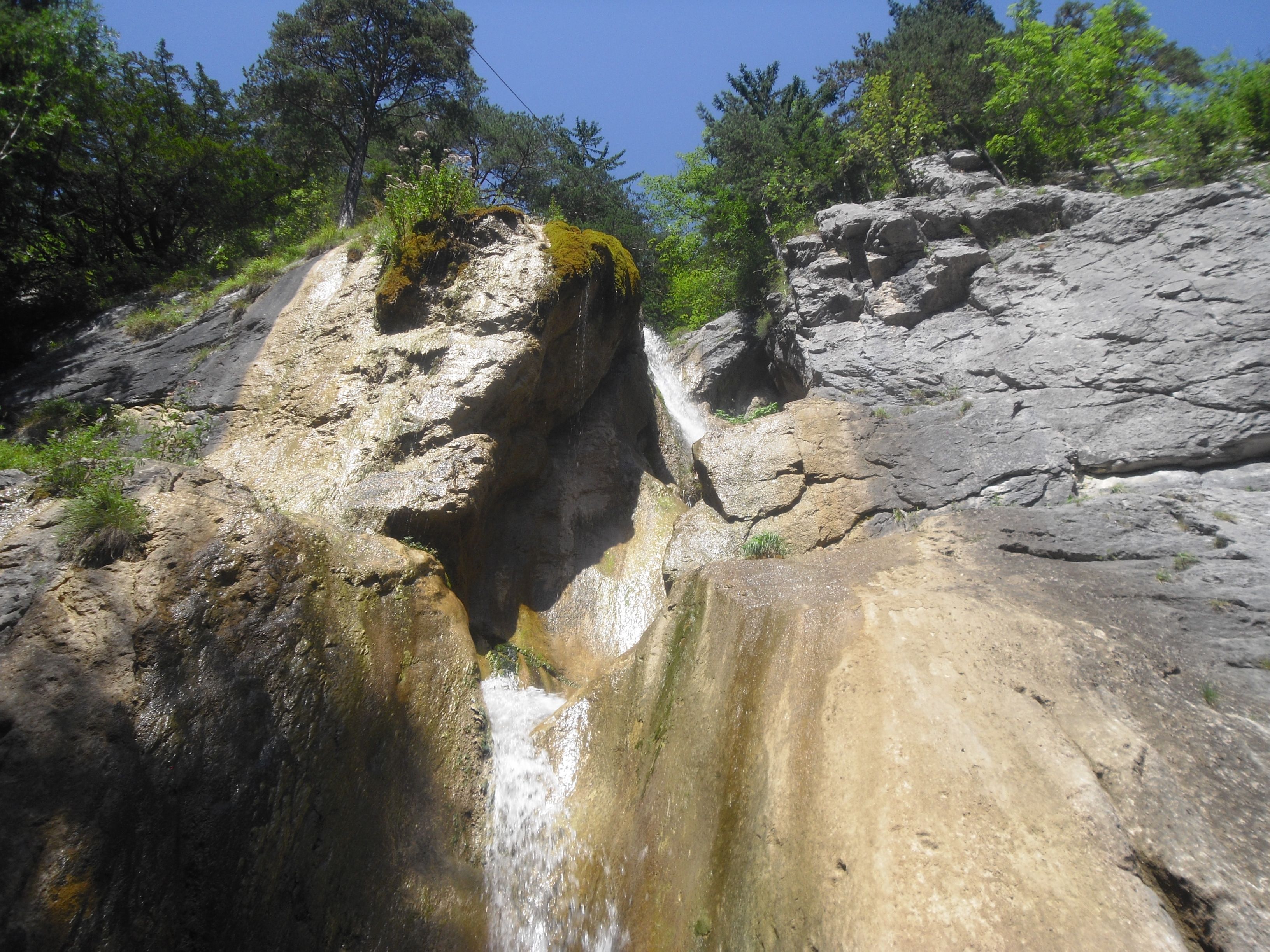 Waterfall in a rocky landscape with trees and blue sky.