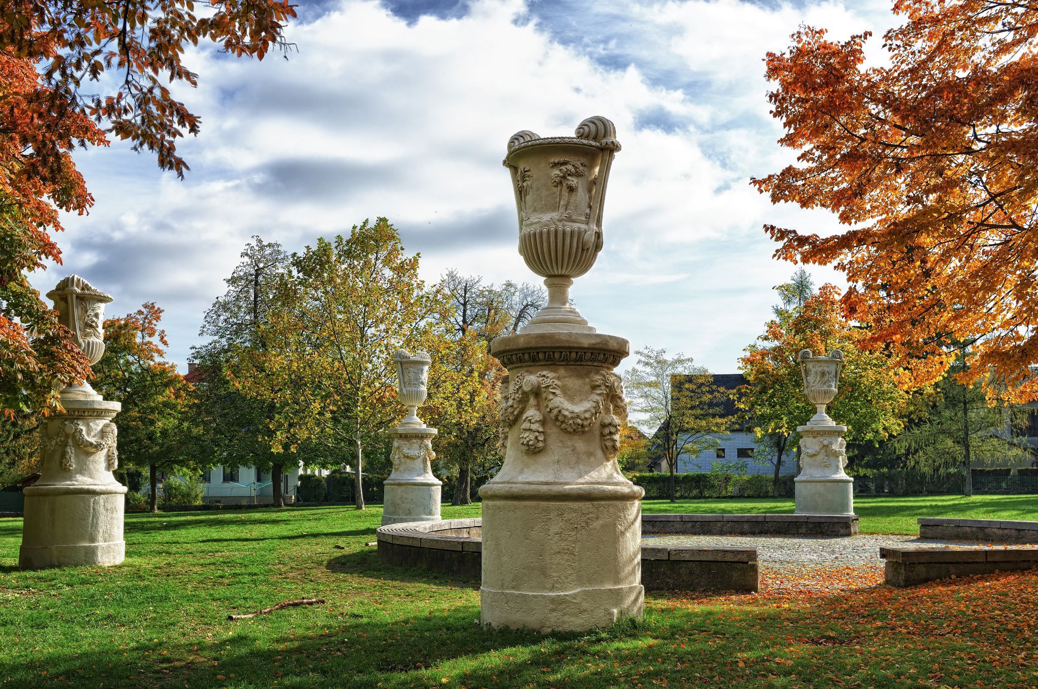 Stone sculptures in an autumnal park with colorful foliage and blue sky.