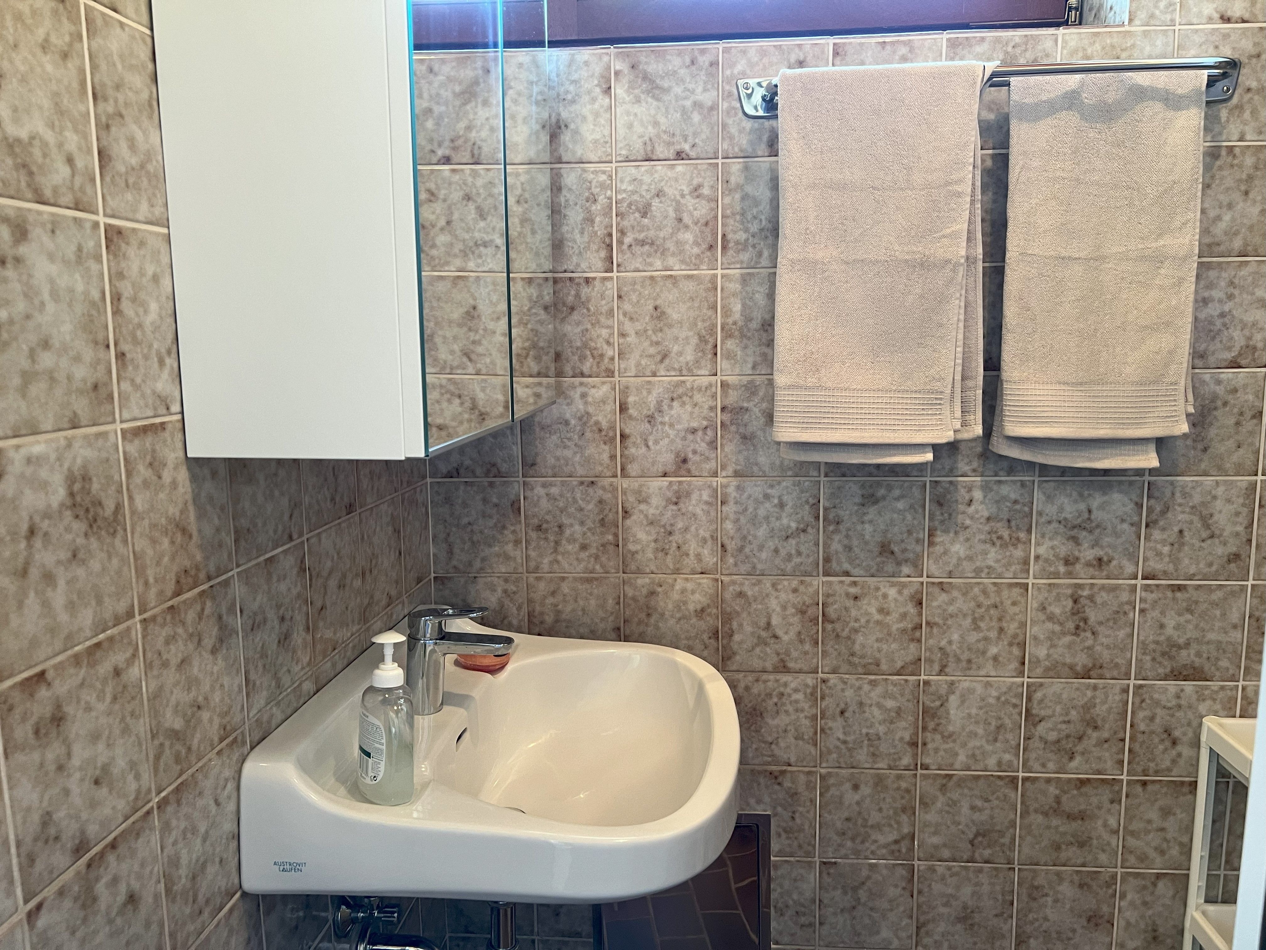 A bathroom with washbasin, mirror, towels and tiles.