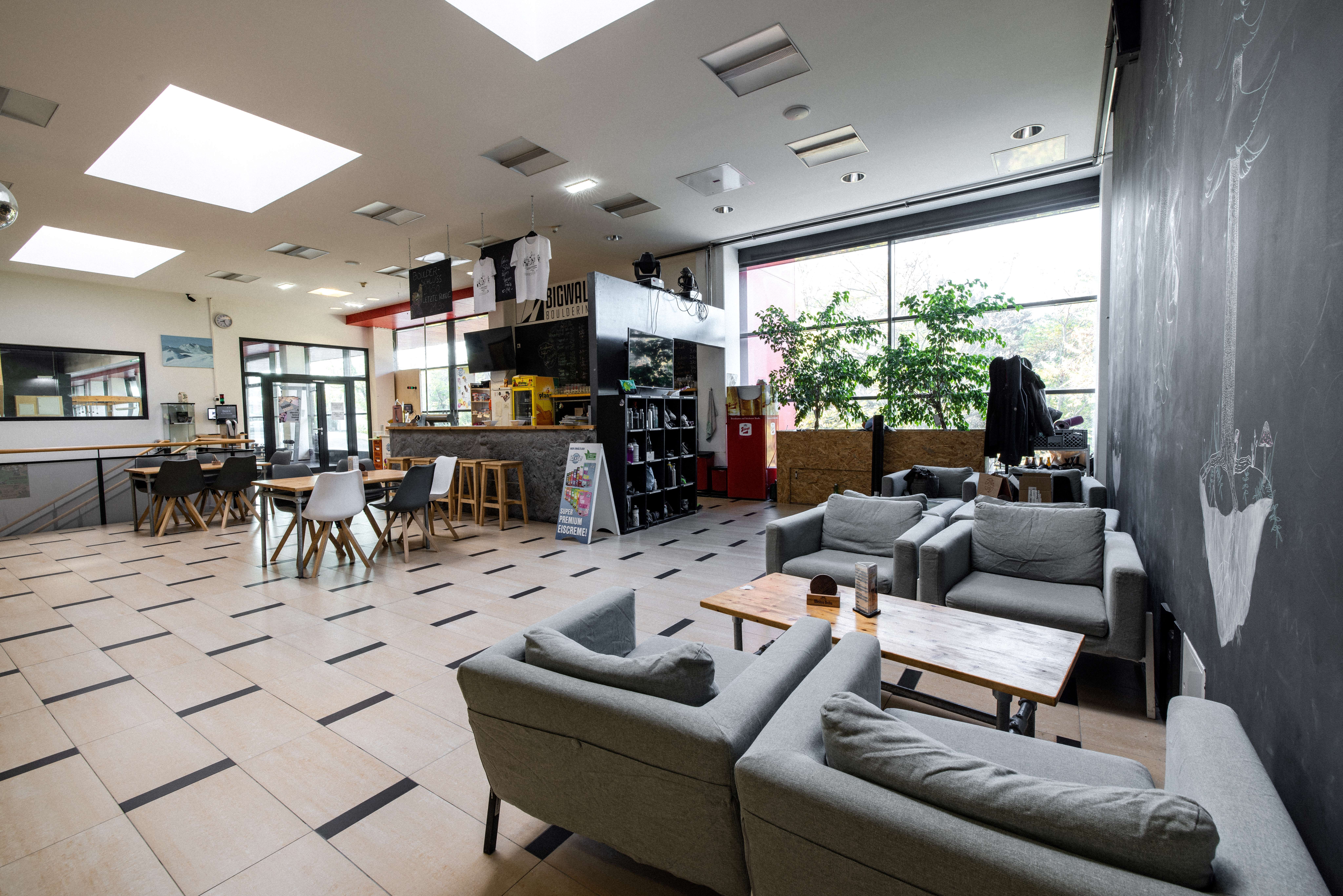 Interior view of a café with gray sofas, wooden tables and a bar in the background.
