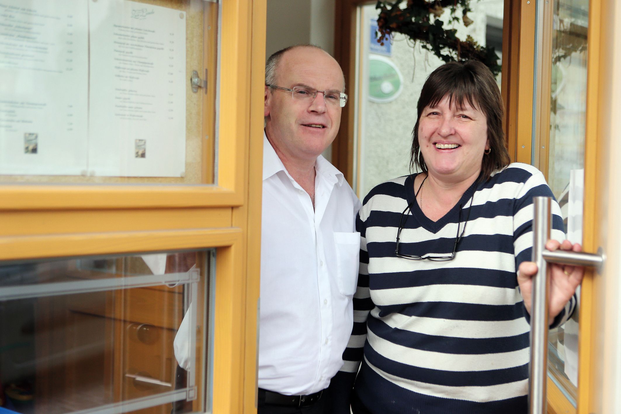 A man and a woman stand smiling in a doorway of a building.
