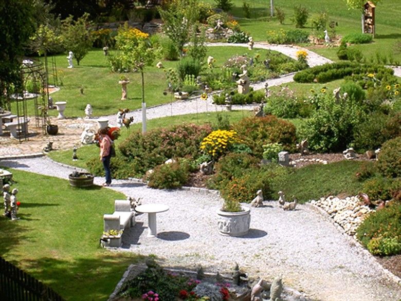 A well-tended show garden with curved paths, flowerbeds and garden figures. A person looks at the plants.